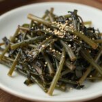 접시에 담긴 깔끔하게 무쳐진 취나물 무침, 통깨가 솔솔 뿌려져 있음