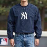 MLB 뉴욕 양키스 로고가 새겨진 네이비색 바람막이를 입은 사람이 데님 팬츠와 함께 캐주얼하게 코디한 모습