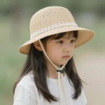 아기밀짚모자 여름 추천 레이스 턱끈이 달린 여아 밀짚모자 클로즈업, 부드러운 밀짚 질감과 장식 디테일이 강조됨