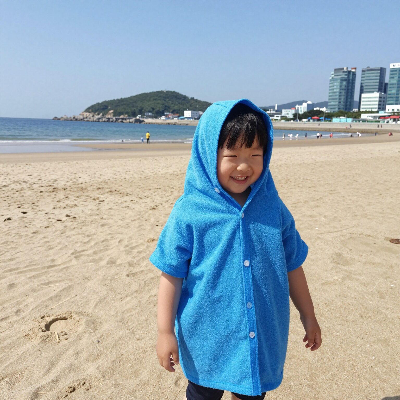 아이가 후드가 달린 비치타올을 입고 해변에서 웃고 있는 모습